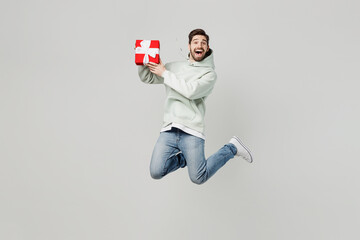 Full body surprised amazed young caucasian man wear mint hoody jump high hold red present box with...