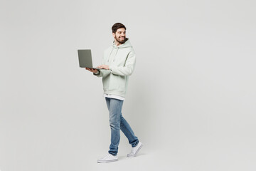 Full body young fun caucasian man wear mint hoody look camera hold use work on laptop pc computer look aside on area isolated on plain solid white background studio portrait. People lifestyle concept.