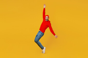 Full body fun young caucasian man wear red hoody hat look camera leaning back stand on toes with outstretched hands isolated on plain yellow color background studio portrait. People lifestyle concept.