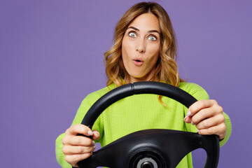 Young cheerful shocked woman 30s wearing casual green knitted sweater hold steering wheel driving car look camera isolated on plain pastel purple background studio portrait. People lifestyle concept.