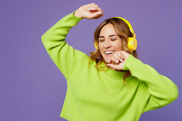 Young woman 30s wearing casual green knitted sweater headphones listen to music dance gesticulating hands have fun isolated on plain pastel purple background studio portrait. People lifestyle concept.