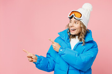 Snowboarder woman wear blue suit goggles mask hat ski padded jacket point index finger aside on mock up isolated on plain pastel pink background. Winter extreme sport hobby weekend trip relax concept. © ViDi Studio