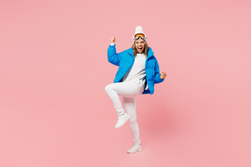 Snowboarder happy woman in blue suit goggles mask hat ski padded jacket do winner gesture raise up leg isolated on plain pastel pink background. Winter extreme sport hobby weekend trip relax concept