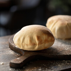 Fototapeta na wymiar Pita bread on wooden cutting board, served with flour over dark table. Bread empty inside of unleavened dough. 
