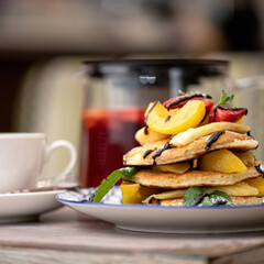 Pancakes with fruit and chocolate topping , decorated with mint on plate for breakfast. Served with fruit tea. Side view. 