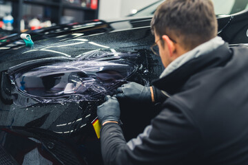 Back view of a caucasian man covering vehicle headlights with film to darken them. Car detailing...