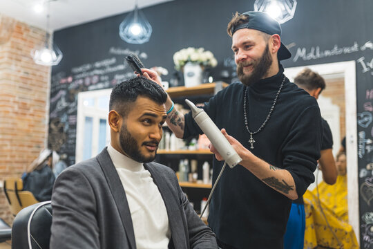 bearded and tattooed barber drying client's hair and shaping it, barbershop medium shot. High quality photo