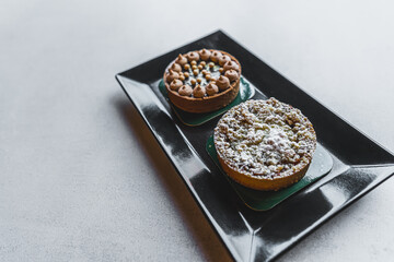 Fruit and chocolate small dessert tarts arranged on black platter on white table. Expensive baked goods. Sweet pastries. Horizontal shot. High quality photo