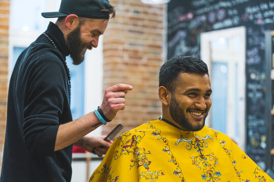 client sitting on the chair and laughing with his barber at the barbershop, medium shot. High quality photo