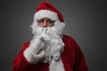 Shot of isolated on grey santa claus posing with finger at his lips.