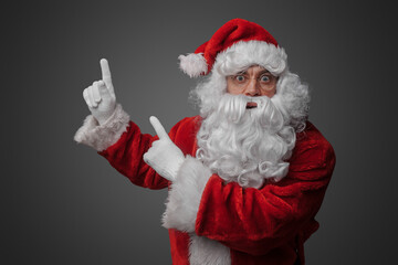 Portrait of old santa claus dressed in red suit pointing up.