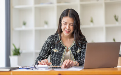 Asian Business woman using calculator and laptop for doing math finance on an office desk, tax, report, accounting, statistics, and analytical research concept