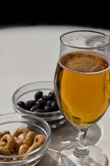 Glass of lager beer with olives and Taralli biscuit snacks on a table