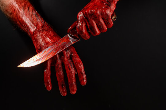 A man wipes a bloody knife with his hand on a black background. 
