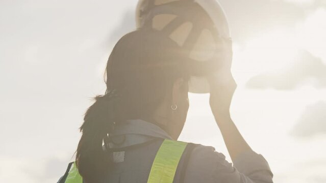 Slow motion of a female engineer putting a construction helmet on at sunset,Work and engineering Concept,Long hair,Close-up