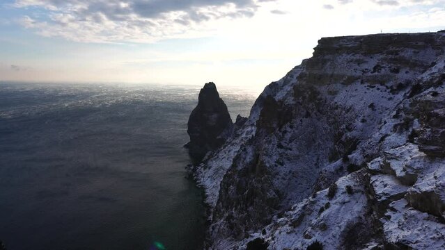 Snow covered rocky cliffs over sea. Winter landscape over the sea bay. Juniper tree under snow. Concept of winter holidays, travel and recreation. Cape Fiolent in Balaklava, Sevastopol, Crimea