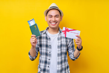 Smiling traveler tourist Asian man in casual clothes with hat holding passport boarding pass...