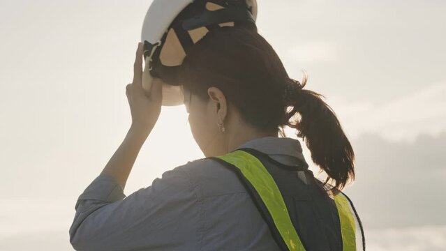 Slow motion of a female engineer putting a construction helmet on at sunset,Work and engineering Concept,Close-up
