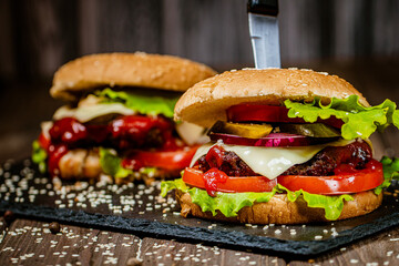 Closeup of delicious burgers with beef, cheese, tomato and lettuce on stone board. Selective focus