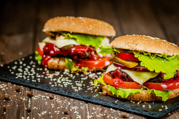 Side view of delicious burgers with beef, cheese, tomato, lettuce on stone board. Selective focus