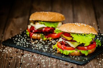 Side view of tasty burgers with beef, cheese, tomato, lettuce on stone board. Selective focus