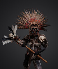 Photo of aztec witch from past with plumed headdress and mask holding staff with skull head.