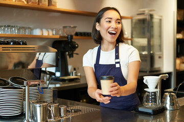 Portrait of smiling asian girl barista, giving out order in cafe, inviting guest to pick up...