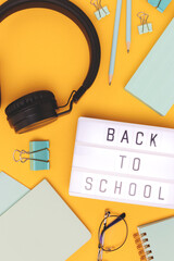 Back to school. Lightbox with letters, headphones and stationery on a yellow background.