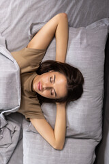 Obraz premium Top view beautiful woman wearing white pajamas sleeping in comfortable bed. Young female resting on soft pillows under warm blanket with closed eyes, relaxing in bedroom at home