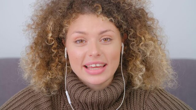 Happy curly woman in headset talking on web camera. Friendly white female greeting people on video call