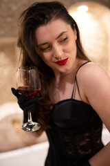 beautiful girl in erotic lingerie sitting in the bathroom with a glass of wine.