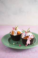 Easter cupcakes with white icing, pink and purple sprinkles and green decor on a pink concrete background. Easter concept.