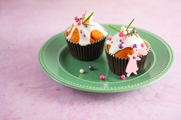 Easter cupcakes with white icing, pink and purple sprinkles and green decor on a pink concrete background. Easter concept.