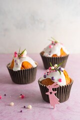 Easter cupcakes with white icing, pink and purple sprinkles and green decor on a pink concrete background. Easter concept.
