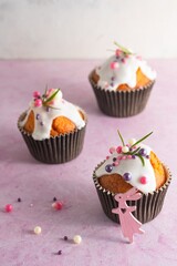 Easter cupcakes with white icing, pink and purple sprinkles and green decor on a pink concrete background. Easter concept.