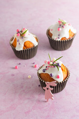 Easter cupcakes with white icing, pink and purple sprinkles and green decor on a pink concrete background. Easter concept.