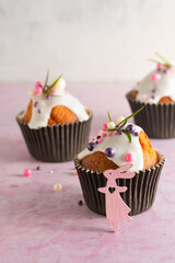 Easter cupcakes with white icing, pink and purple sprinkles and green decor on a pink concrete background. Easter concept.