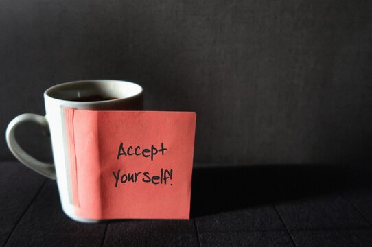 White mug coffee cup on dark gray wallpaper with copy space , pink note with text written ACCEPT YOURSELF , concept of self acceptance , ability to embrace all facets of oneself , positive or negative