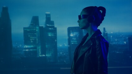 Portrait of cyberpunk girl with a smartphone in a glasses and headphones. Beautiful young woman on the background of city scyscrapers. © Acronym