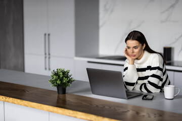 Fototapeta premium Portrait of a pretty young woman studying while sitting at the table with laptop at home