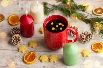 festive Christmas tea in a red cup with a knitted pattern on the table next to cookies, spices and candles
