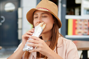 A female in a hat eating a kebab in a street cafe