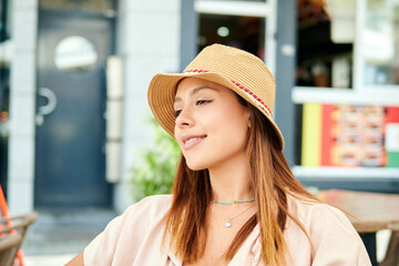A beautiful Hispanic female in a hat sitting in a cafe on a sunny day