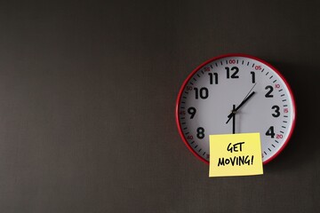 Wall clock on gray office wallpaper with handwritten note GET MOVING!, concept of having difficulty setting aside exercise time, reminder for health improvement by being more physically active