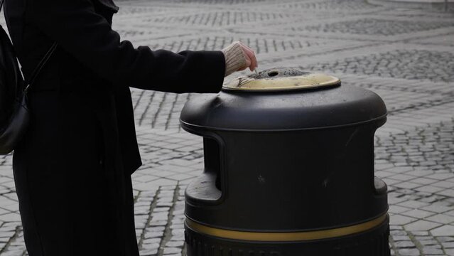 Female Put Out Cigarette In Ashtray On The Street. Garbage Can With Pavement Background