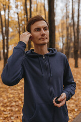 Naklejka na ściany i meble Sportsman listening to music in wireless earphones during running training in autumn park 
