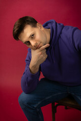 young man in a purple hoodie posing at the camera, look at the camera on a red background