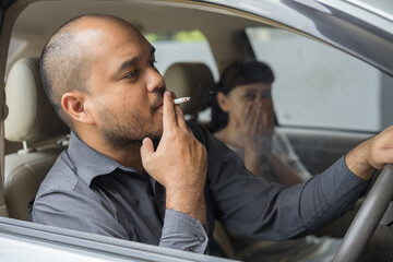 Husband smoking cigarette and wife choking of smoke. Man smoking cigarette and woman is covering...
