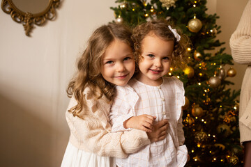 Merry Christmas and Happy Holidays. Smiling sisters playing with a Christmas decoration, Christmas tree on the background