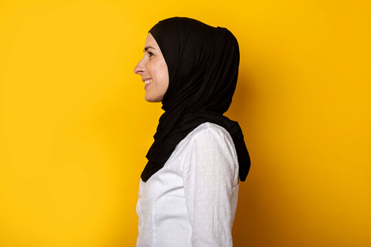 Young Muslim Woman In Hijab Looks To The Side And Smiles On A Yellow Background. Banner. Profile Shot, Side View